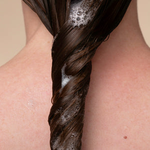 Close-up of a person with a braided hair section covered in soap suds.
