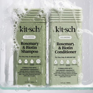Kit-Sch Rosemary & Biotin Shampoo and Conditioner bottles with soap suds on a clear background