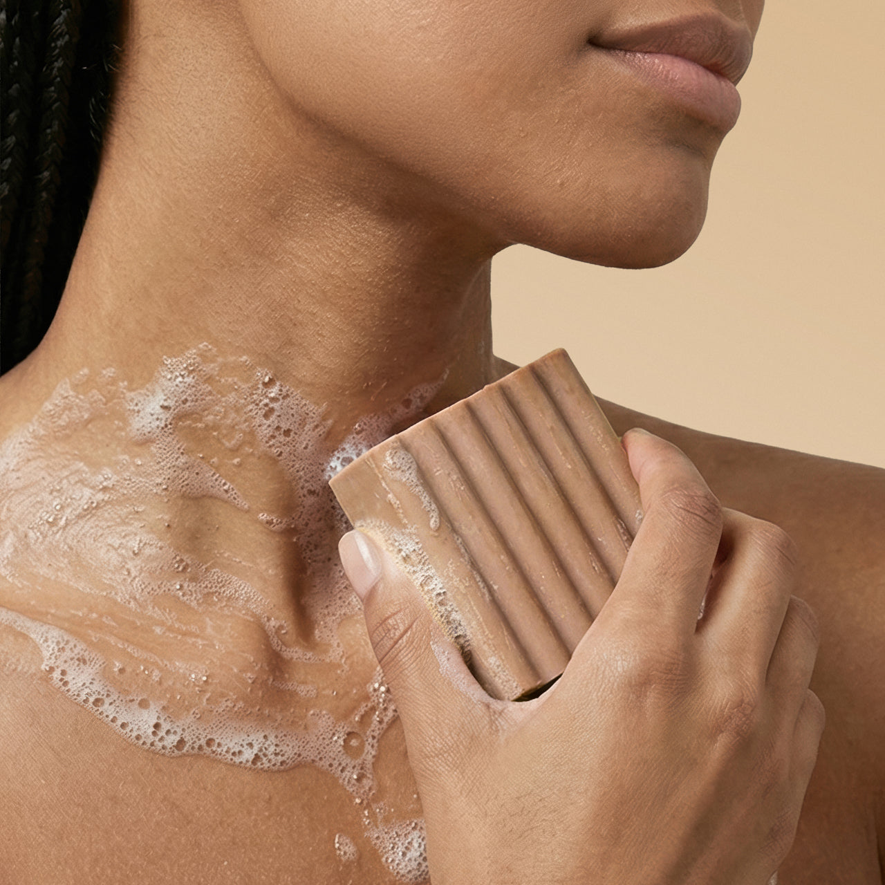 Woman lathering Kitsch Warm Sugar Body Wash Bar on shoulder with sudsy foam on a beige background
