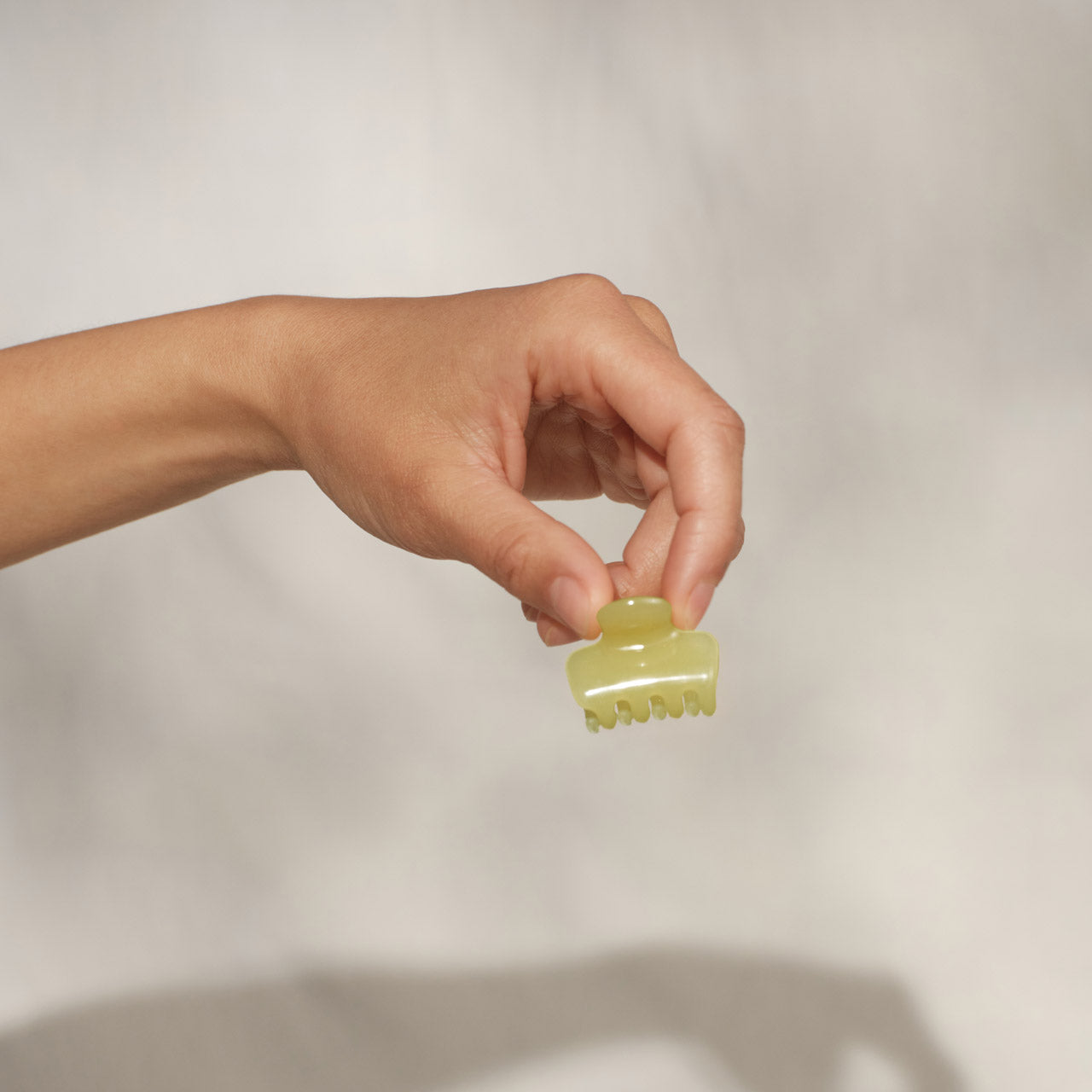 Hand holding single KITSCH Butter Yellow Jelly Cloud Clip Mini between fingers — close-up detail shot on cream background — mini claw clip design, jelly texture in butter yellow — All-Day Hold, Made from Recycled Materials — KITSCH Pearlized Cream & Butter Yellow Jelly Cloud Clips Mini 8pcs