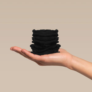 Stack of kitsch black petal hair elastics in a hand against a beige plain background