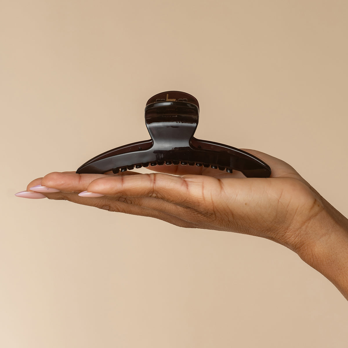 Hand displaying kitsch translucent Black Arched Claw Clip - Large from the front against a beige background