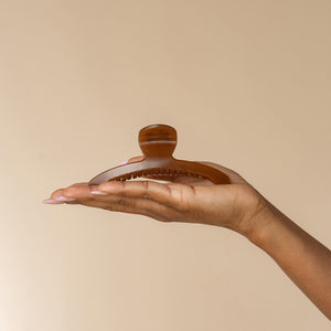 Hand displaying kitsch translucent Mocha Arched Claw Clip - Large from the front against a beige background