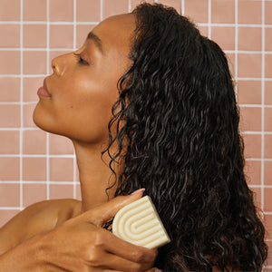 female model with shoulder-length curly hair using the kitsch coconut oil conditioner bar