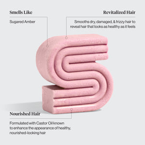 Pink Kitsch castor oil solid shampoo bar with text describing its benefits on a light gray background. Benefits are: Smells like sugared amber, revitalized hair smooths dry, damaged, and frizzy hair to reveal hair that looks as healthy as it feels, and Nourished hair formulated with castor oil known to enhance the appearance of healthy, nourished-looking hair