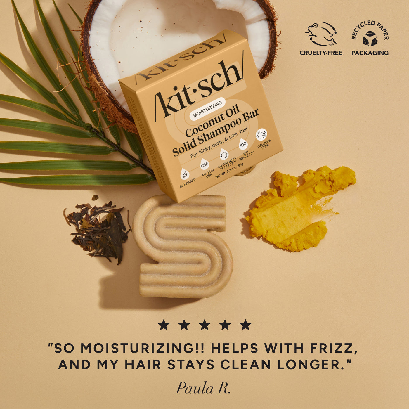 Kitsch coconut oil shampoo bar with palm leaf and coconuts on a beige background.  There is a Leaping Bunny Cruelty-free badge and a Recycled paper packaging badge on the top right corner. On the bottom of the image, there is a customer review that says "so moisturizing! helps with frizz and my hair stays clean longer"