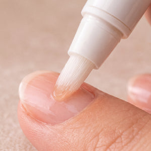 KITSCH Nourishing Nail & Cuticle Oil - Honey & Milk — close-up of a brush-tip applicator gliding oil onto a bare fingernail cuticle against a soft beige background — brush-tip pen, mess-free — brush oil directly onto each cuticle and around the nail